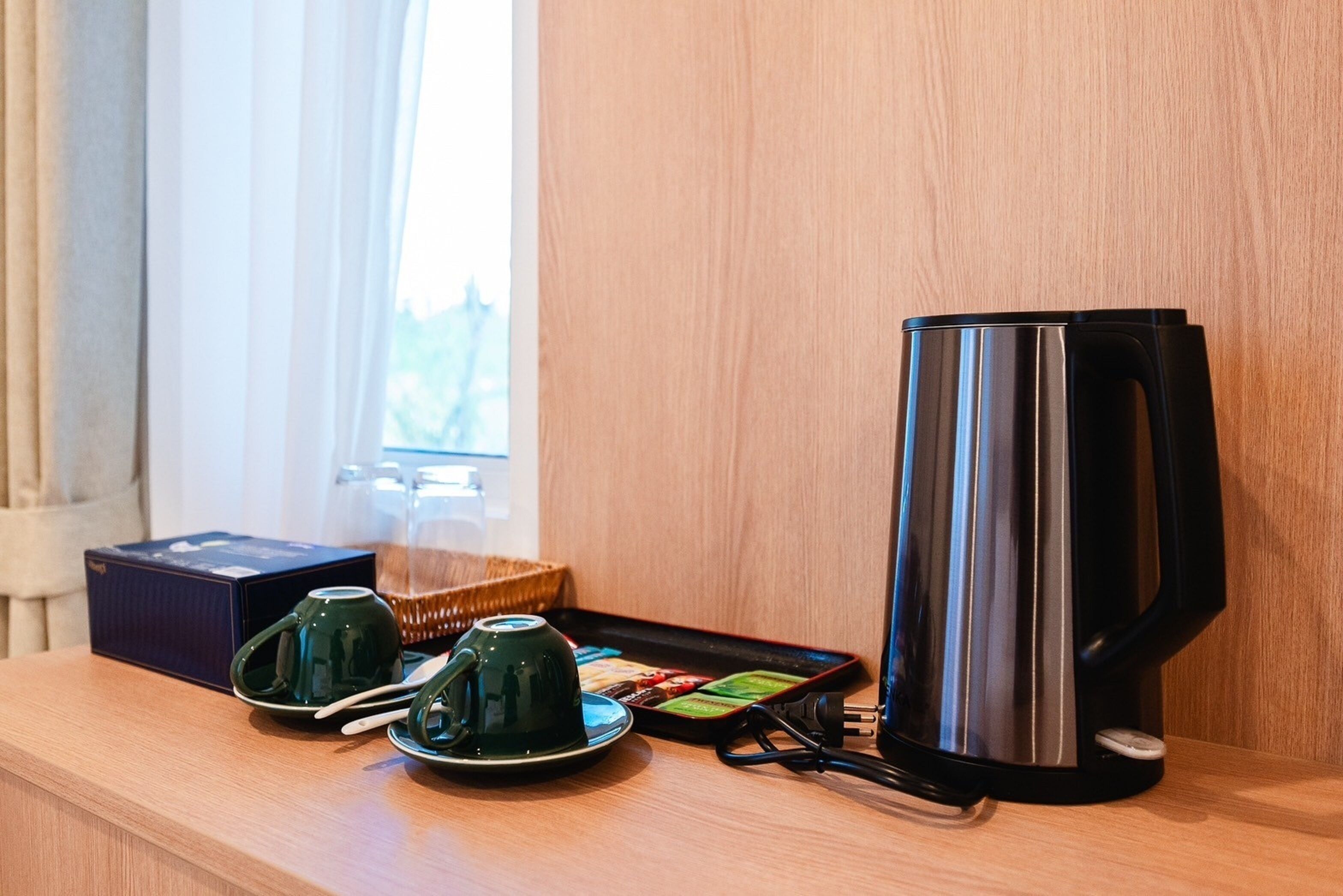 A coffee station with a black electric kettle, two green tea cups, and a tray of assorted teas.