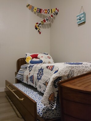 Une chambre avec un lit en bois, une couvre-lit matelassé, une décoration murale représentant des drapeaux et une petite ancre décorative.