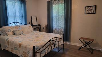 A bedroom with a bed, a chair, a small table, and a picture on the wall.