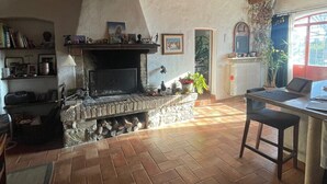 Ein rustikales Interieur mit Kamin aus Stein, Holzbalken und Fliesenboden.