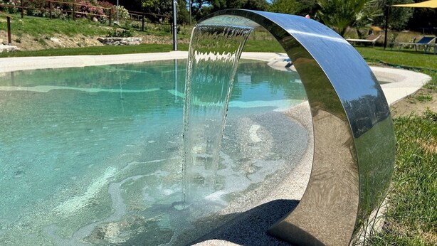 Ein klares Schwimmbecken mit einer geschwungenen, metallischen Wasserspielfeatur.