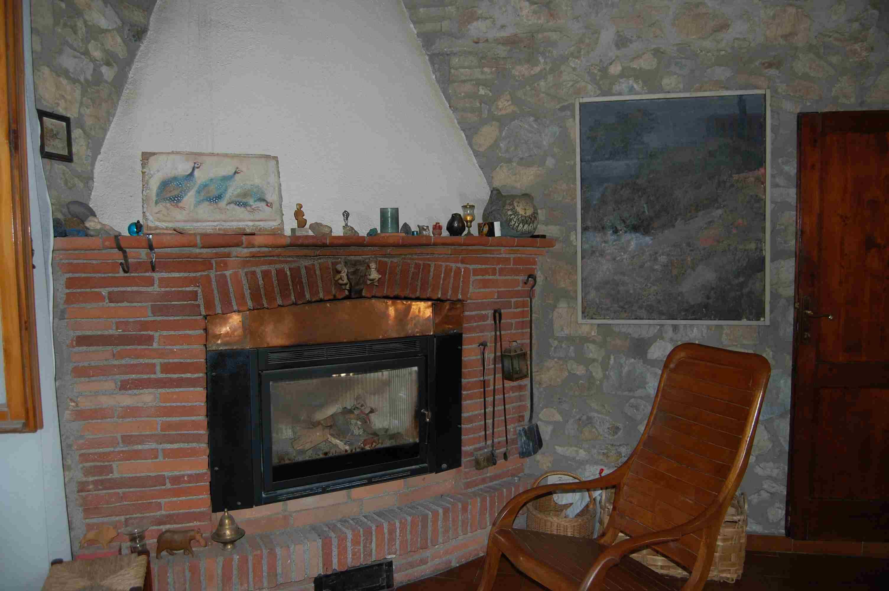 Una chimenea de ladrillo con una chimada, una silla de madera y una pared de piedra con un cuadro.
