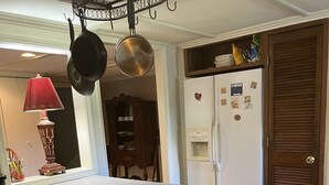 A kitchen with a central island, wooden stools, a hanging pot rack, and a refrigerator with magnets. - Southern Charm and Convenience: Perfect VRBO Retreat Near Ole Miss and Tupelo. (Pontotoc)