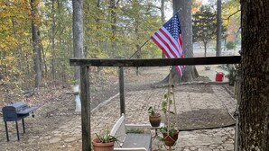 A wooden bench with potted plants, an American flag, and a stone pathway in a wooded area. - Southern Charm and Convenience: Perfect VRBO Retreat Near Ole Miss and Tupelo. (Pontotoc)