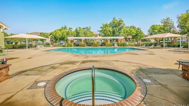 Una piscina amb un banyera d'hidromassatge, envoltada d'zones d'seure cobertes i un marc de maó.
