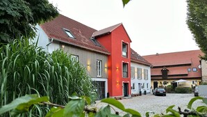 A traditional European building with a red and white facade, a cobblestone courtyard, and surrounding greenery. - At the gateway to Franconian Switzerland - Apartment with bedroom (Eckental)