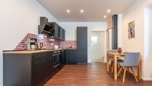 A modern kitchen with a brick backsplash, black cabinetry, and a wooden dining table with chairs. - At the gateway to Franconian Switzerland - Apartment with bedroom (Eckental)