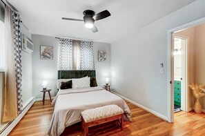 A bedroom with a bed, a ceiling fan, a window with curtains, a bedside table, and a nightstand. - Cincinnati 2BR Corporate Stay, Garage Parking (Cincinnati)
