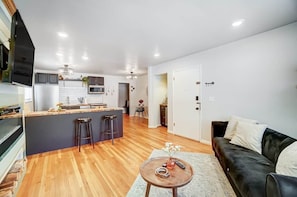 A modern kitchen with a central island, a dining area with a table and chairs, a black leather sofa, and a small round table with a vase and remote controls. - Cincinnati 2BR Corporate Stay, Garage Parking (Cincinnati)