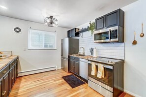 A modern kitchen with stainless steel appliances, a wooden floor, and a window with blinds. - Cincinnati 2BR Corporate Stay, Garage Parking (Cincinnati)