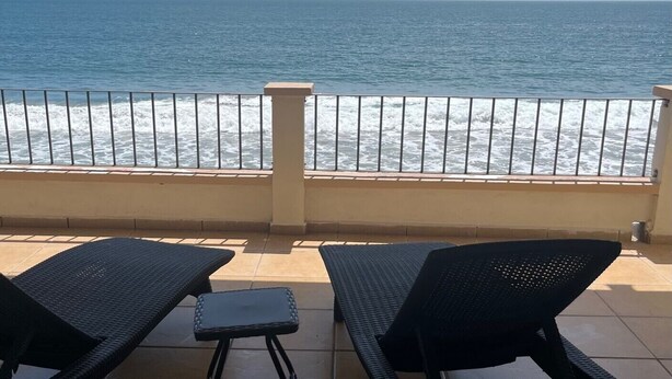 Un balcone con due poltrone nere e un tavolino, affacciato sull'oceano con le onde che si infrangono sulla spiaggia.