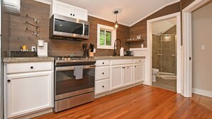 A modern kitchen with stainless steel appliances, white cabinetry, and a wooden floor. - Close to Town - Pet Friendly Cabin w/ Fire Pit (Lake George)