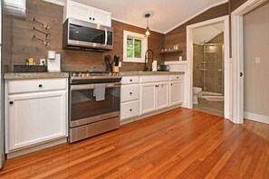 A modern kitchen with stainless steel appliances, white cabinetry, and a wooden floor. - Close to Town - Pet Friendly Cabin w/ Fire Pit (Lake George)