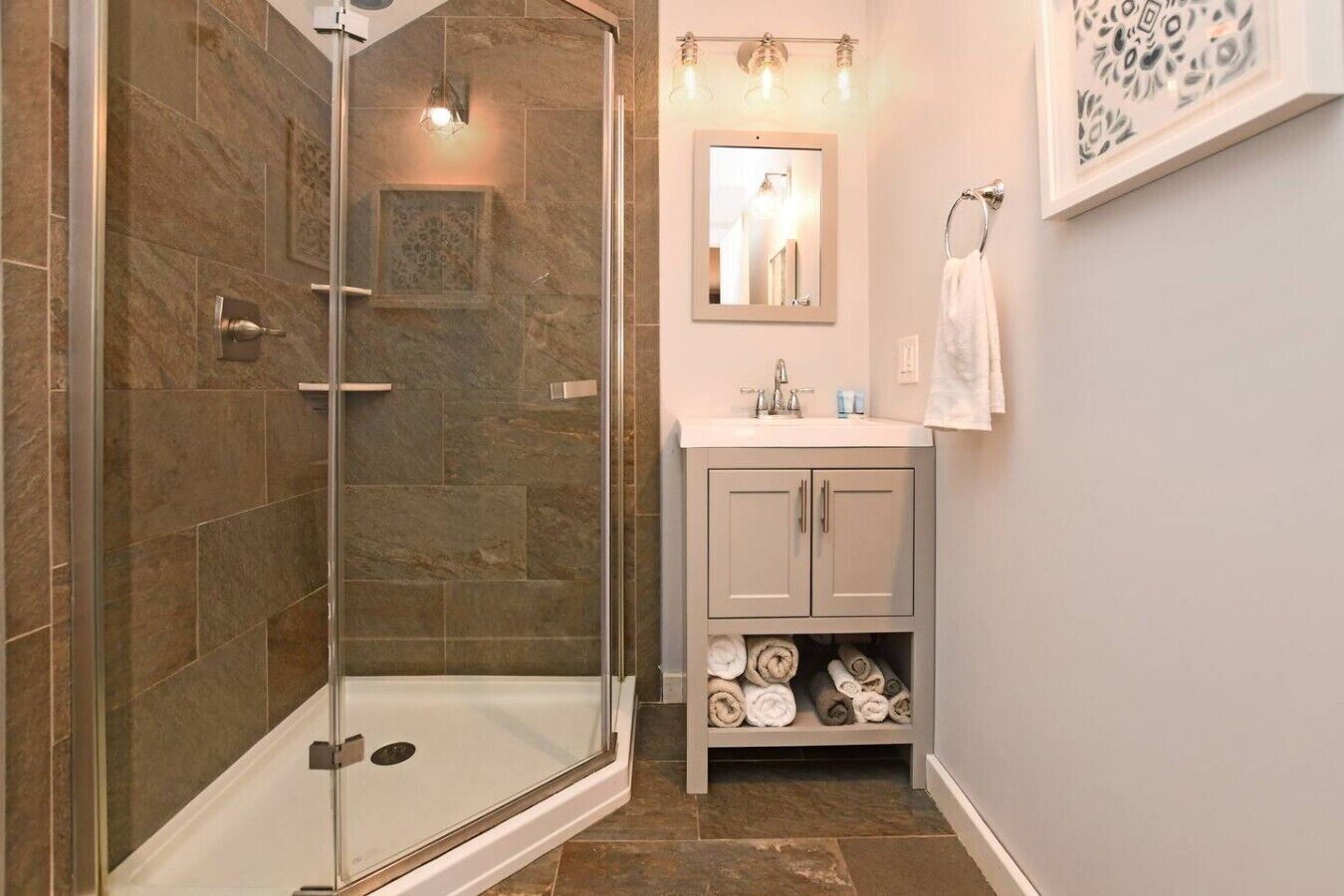 Une salle de bain avec une douche à parois de verre, un lavabo avec un miroir au-dessus et un porte-serviettes.