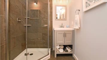 Une salle de bain avec une douche à parois de verre, un lavabo avec un miroir au-dessus et un porte-serviettes.