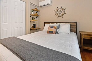 Een slaapkamer met een bed, een hoofdeinde, een aan de muur bevestigd decoratieve schep, een plank met boeken en een potplant, en een grijs vloerkleed.