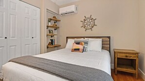 A bedroom with a bed, bedside tables, a wall-mounted air conditioner, and a decorative ship's wheel. - Close to Town - Pet Friendly Cabin w/ Fire Pit (Lake George)