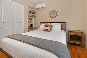 A bedroom with a bed, bedside tables, a wall-mounted air conditioner, and a decorative ship's wheel. - Close to Town - Pet Friendly Cabin w/ Fire Pit (Lake George)