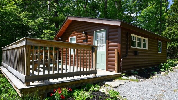 A small cabin with a wooden deck, a door, and windows. - Close to Town - Pet Friendly Cabin w/ Fire Pit (Lake George)