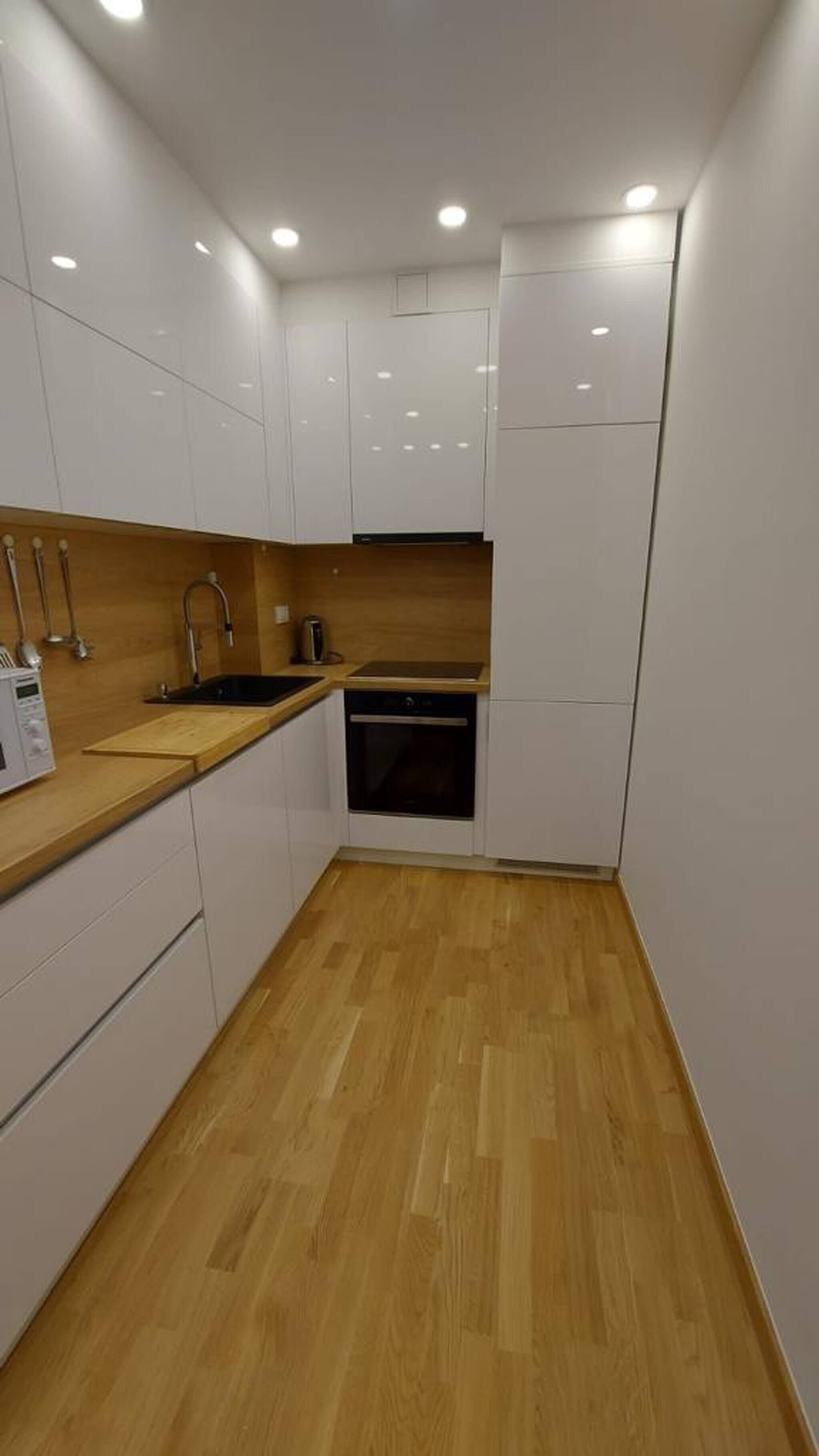 A compact kitchen with white cabinets, a wooden countertop, a sink, a stove, and a dishwasher.