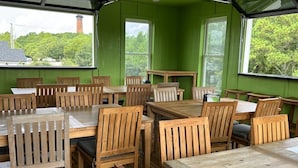 A dining area with wooden tables and chairs, large windows, and a view of trees and a building. - Welcome to Waves of Fun Single Level, Dog Friendly (Corolla)
