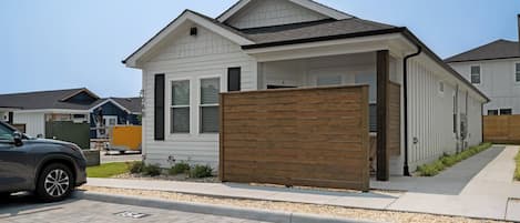 Una casa moderna de un solo piso con garaje, cerca viva de madera y entrada pavimentada.