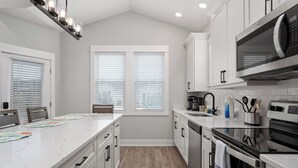 A modern kitchen with white cabinetry, a large island with a marble countertop, and a built-in microwave. - Welcome to Waves of Fun Single Level, Dog Friendly (Corolla)