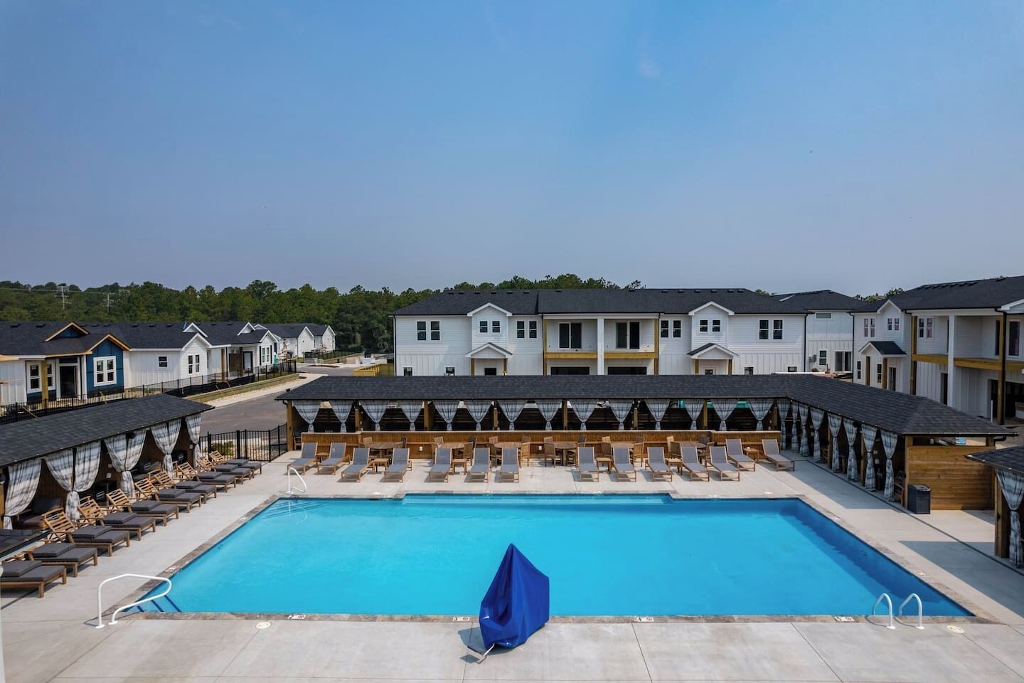 A swimming pool with lounge chairs and a covered area, surrounded by multi-story buildings.