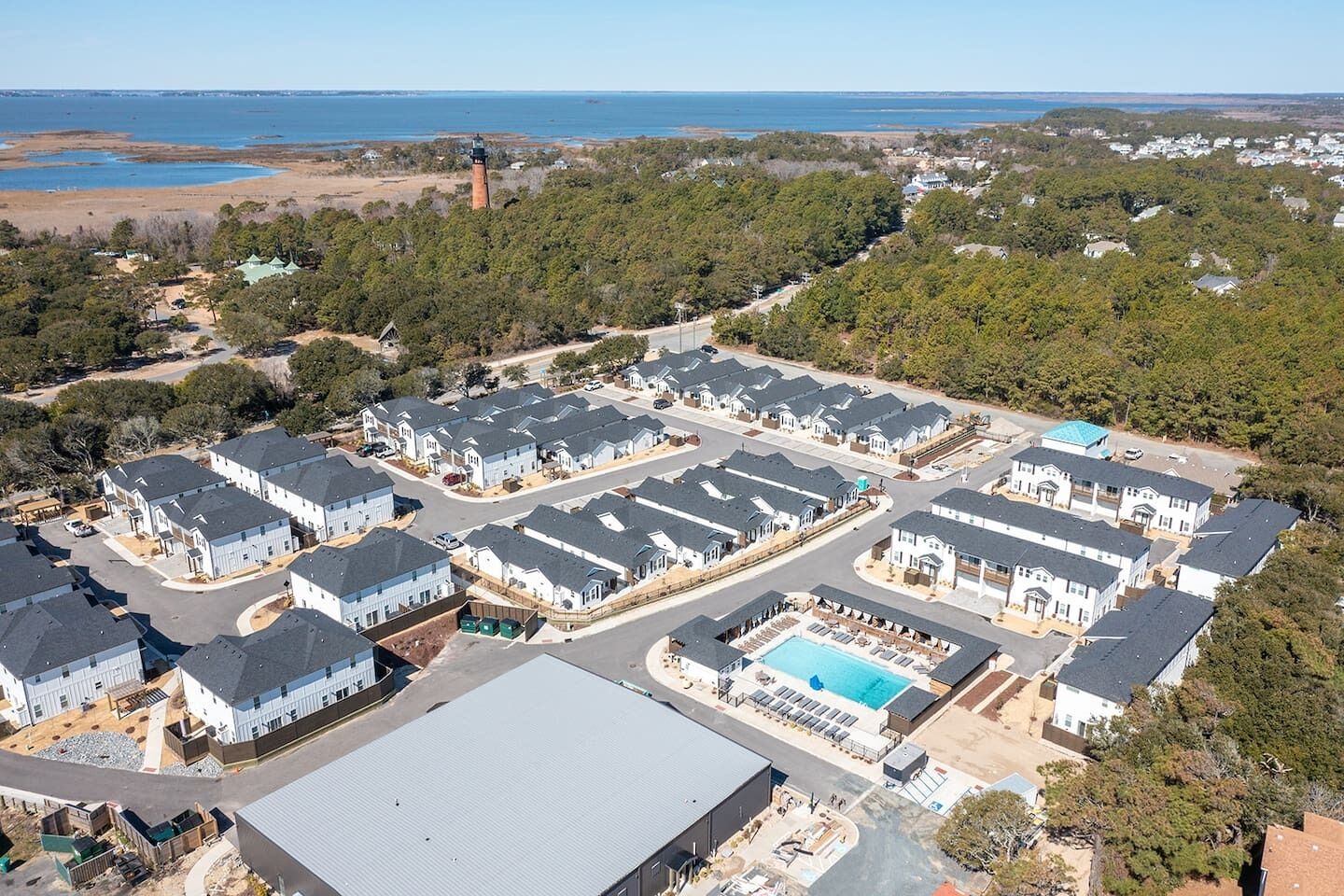 A residential area with multiple houses, a swimming pool, and a lighthouse in the background.