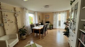 Un coin repas avec une table et des chaises, un canapé, un meuble avec des livres et une plante en pot.