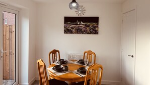 Un coin repas avec une table ronde, quatre chaises en bois, de la vaisselle noire et un luminaire suspendu.