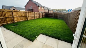 Un jardin avec une pelouse verdoyante, une clôture en bois et une maison en arrière-plan.