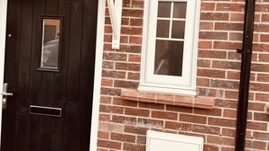 Une maison en briques avec une porte en bois sombre, une petite fenêtre et une boîte électrique blanche.