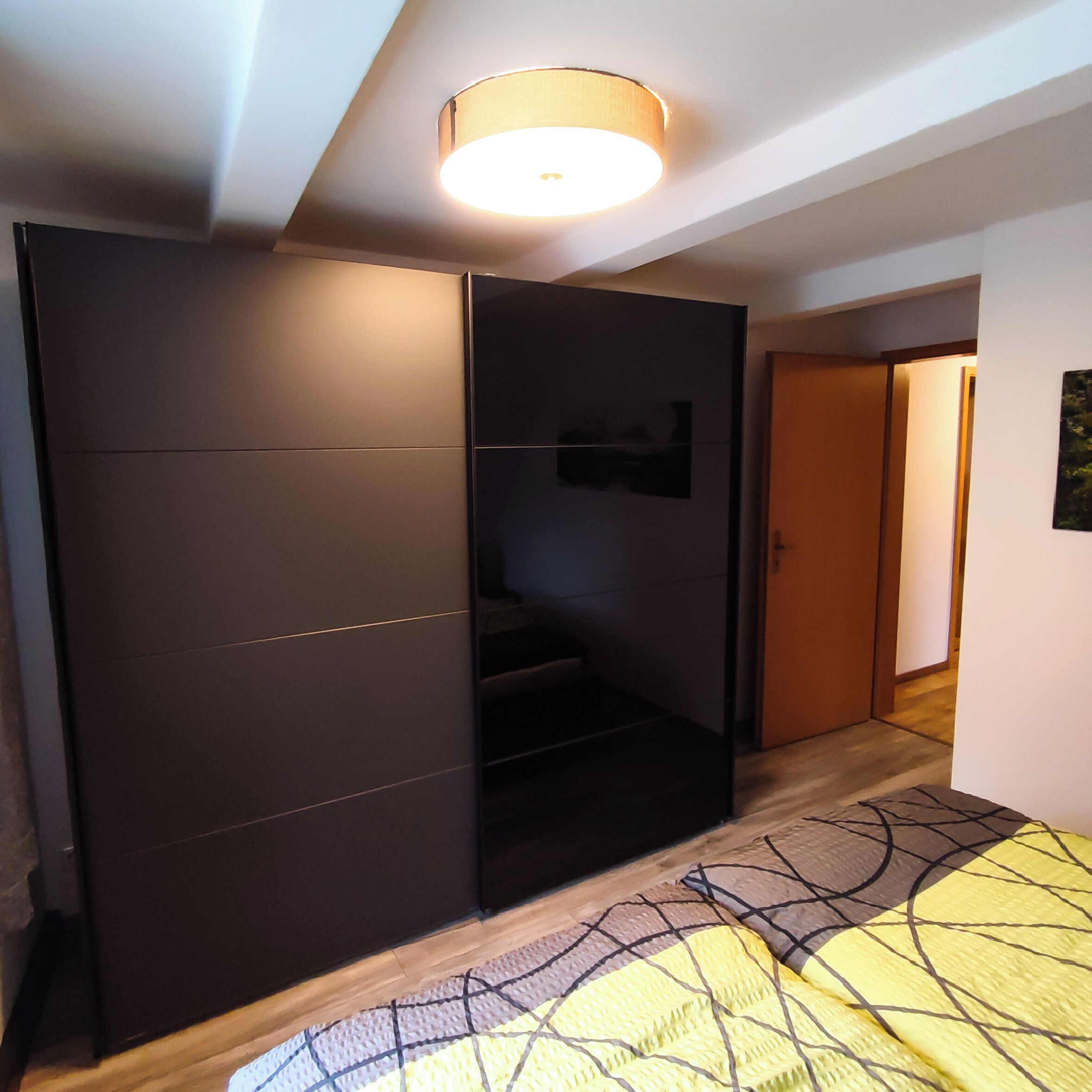 Een moderne slaapkamer met een schuifdeurkast, een bed met een geborreld sprei en een plafondlamp.