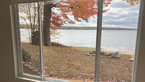 A room with a large window overlooking a lake, a stone wall, and a wooden deck. - Lake life at its finest with nearby outdoor adventures! Hunters and ORV welcome! (Baldwin)