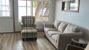 A spacious living room with a plaid armchair, a beige sofa, and a round coffee table. - Lake life at its finest with nearby outdoor adventures! Hunters and ORV welcome! (Baldwin)