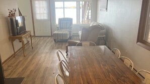 A dining area with a wooden table and chairs, a television on a side table, and a view through a door to the outside. - Lake life at its finest with nearby outdoor adventures! Hunters and ORV welcome! (Baldwin)