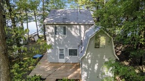 A two-story house with a deck and a small shed, surrounded by trees and a body of water. - Lake life at its finest with nearby outdoor adventures! Hunters and ORV welcome! (Baldwin)