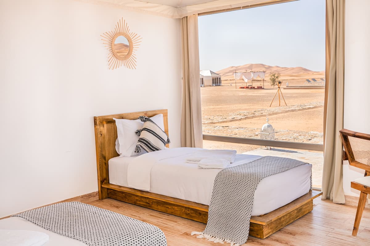 A bedroom with a wooden bed, a view of the desert, and a sun-shaped wall decoration.