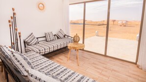 Una habitació amb un sofà, una taula de fusta petita i una gran porta corredissa de vidre que dona a una vista del desert.