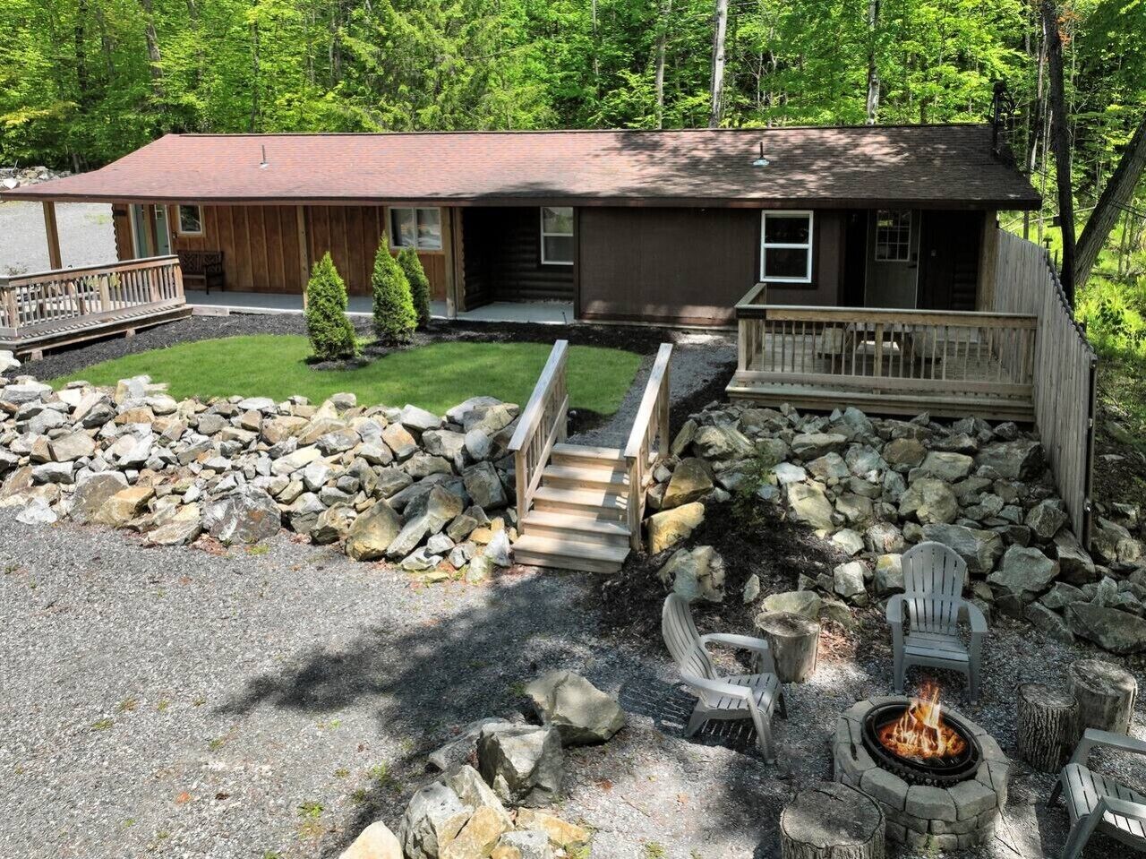 A cabin with a deck, a fire pit, and a stone wall.