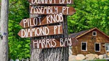 A wooden signpost with multiple directional arrows pointing to various locations such as Bolton Landing, Kattskill Bay, and Harris Bay.