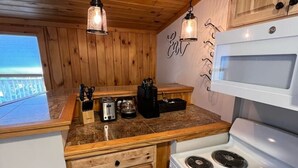 A kitchen with wooden cabinets, a white stove, and hanging pendant lights. - Walk to Beach - Pet friendly Cabin w/ Workspace (Lake George)