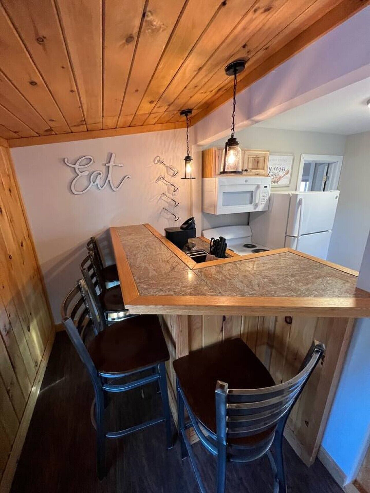 A compact kitchen with a central island, wooden ceiling, and a wall-mounted light fixture.