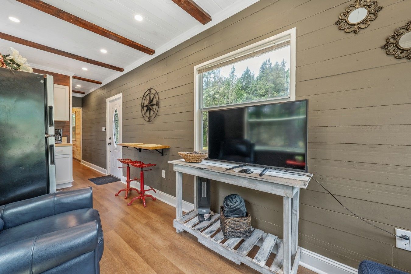 A living room with a TV, a wooden table, a red stool, and a sofa.