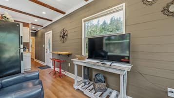 A living room with a TV, a wooden table, a red stool, and a sofa.