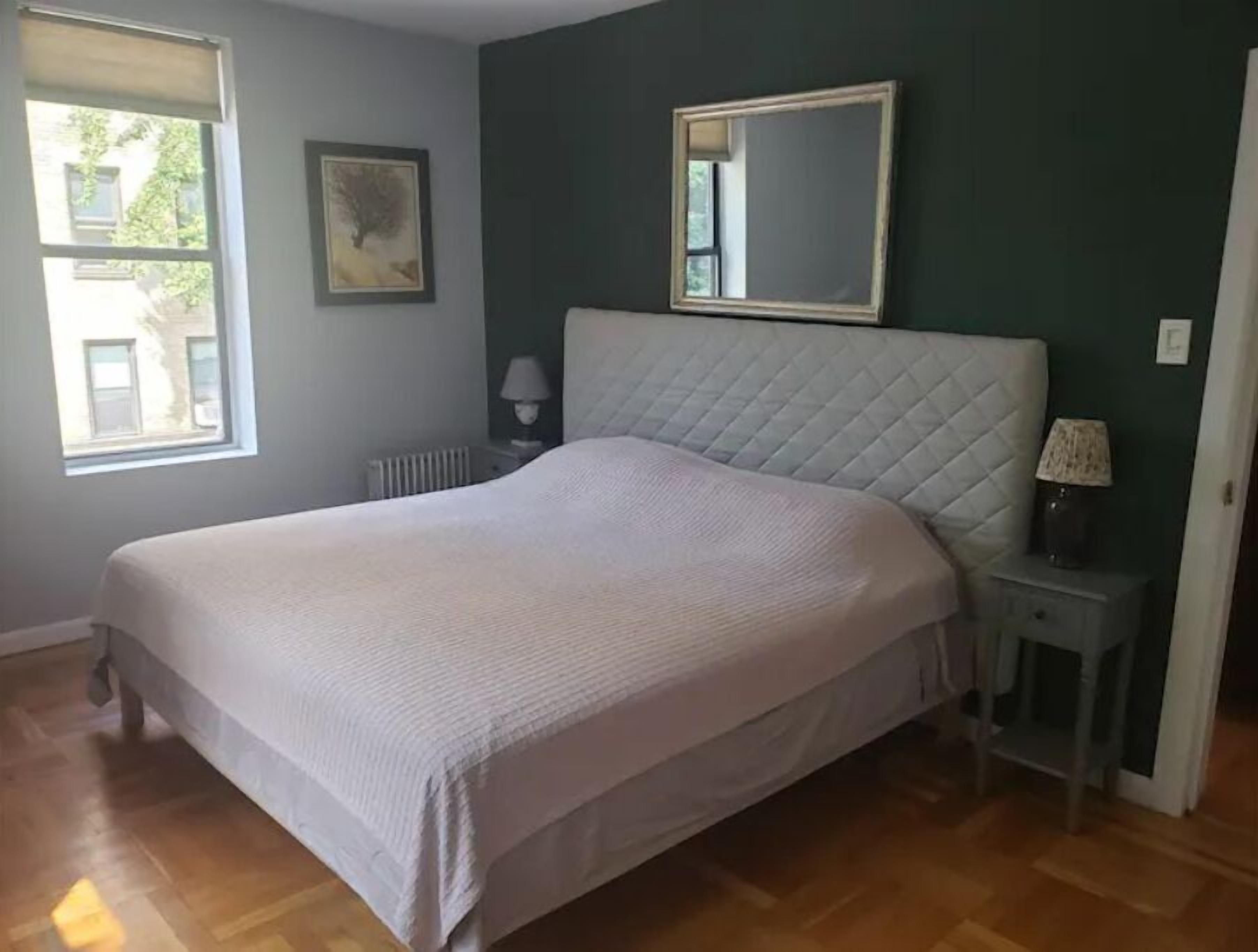 A bedroom with a large bed, a nightstand, a mirror, and a window.