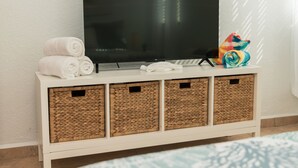 A white entertainment unit with a flat-screen TV, three woven baskets, and rolled towels. - Cozy Condo in Cabo Rojo (Cabo Rojo)