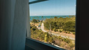 A view from a window overlooking a coastal area with palm trees and a road. - Cozy Condo in Cabo Rojo (Cabo Rojo)