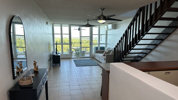 A spacious living area with a staircase, large windows, and a ceiling fan. - Cozy Condo in Cabo Rojo (Cabo Rojo)